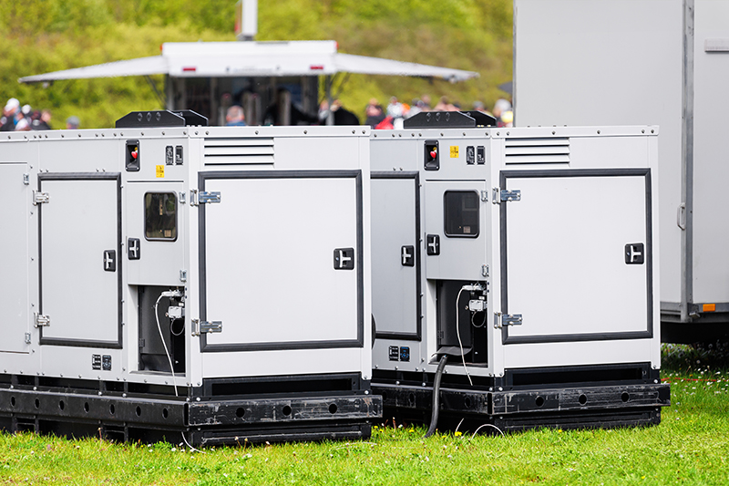 Set two large portable industrial power fuel generator green lawn at commercial event outdoors clear blue sky background. Mobile electricity supply energy plant unit backup equipment rent service